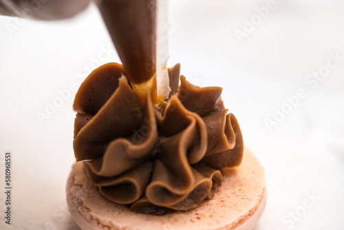 the pastry chef squeezes the filling onto macarons cookies. close-up. home bakery concept.