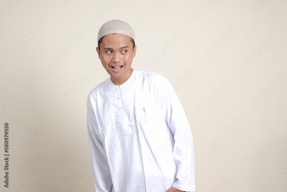 Portrait of attractive Asian muslim man in white shirt showing shocked expression and looking aside. Isolated image on gray background Portrait of attractive Asian muslim man in white shirt showing shocked expression and looking aside. Isolated image on gray background
