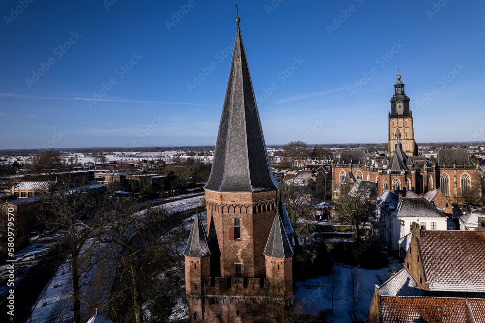 Cinematic aerial view of Drogenapstoren in medieval Hanseatic Dutch tower town Zutphen in the Netherlands with historic heritage buildings covered in snow in the background
