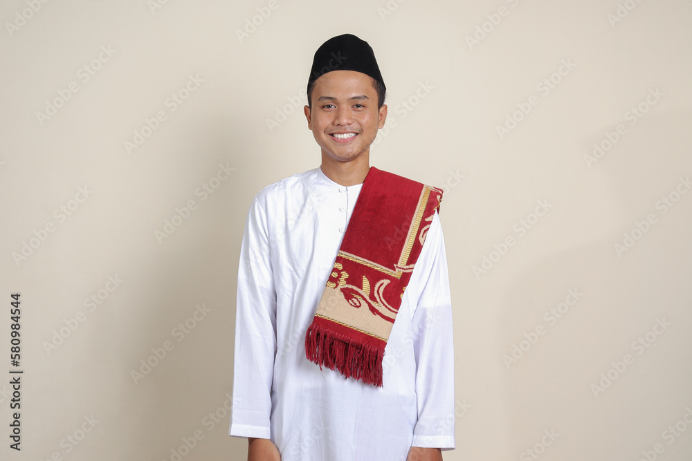 Portrait of attractive Asian muslim man in white shirt feeling confident, smiling and looking at camera. Isolated image on gray background Portrait of attractive Asian muslim man in white shirt feeling confident, smiling and looking at camera. Isolated image on gray background