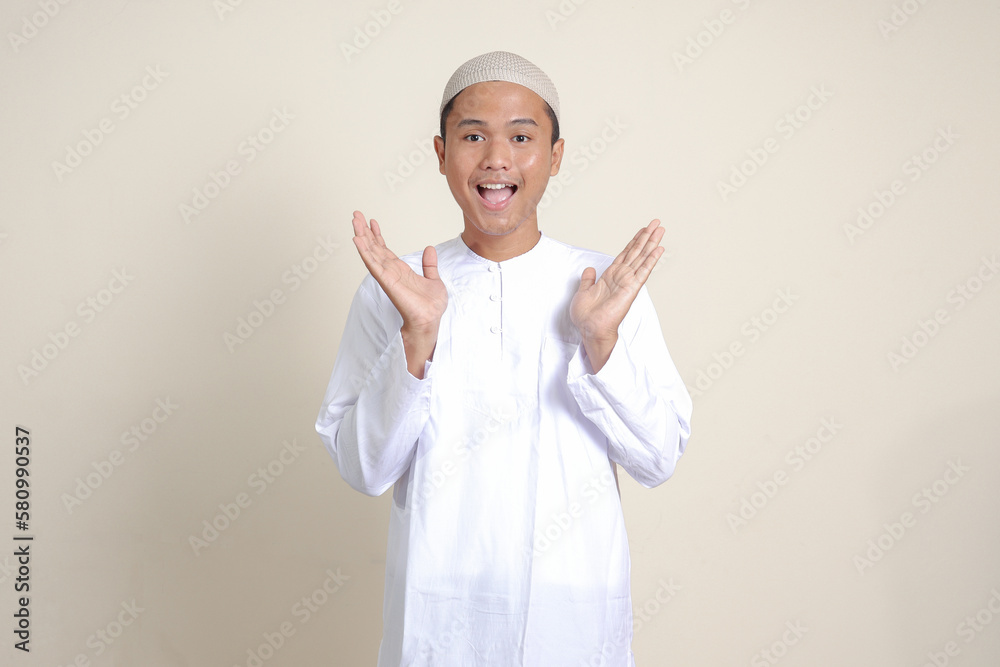 Portrait of attractive Asian muslim man in white shirt pulling hands towards camera, inviting someone to come inside, welcoming gesture. Isolated image on gray background Portrait of attractive Asian muslim man in white shirt pulling hands towards camera, inviting someone to come inside, welcoming gesture. Isolated image on gray background