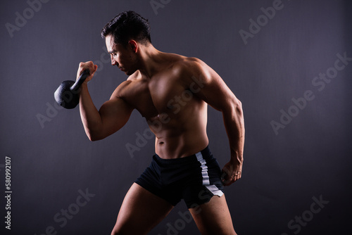 Hispanic male athlete working out with kettlebell on grey background. Crossfit workout theme. © Ivan Zelenin