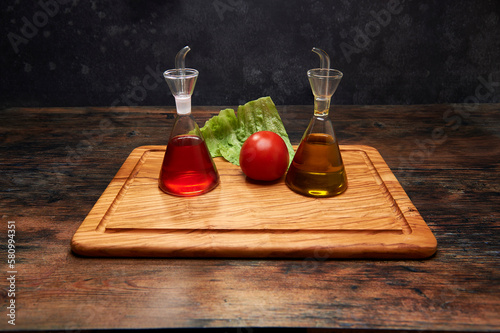 Glass cruet and oil can on olive cutting board with a lettuce leaf and a tomato photo