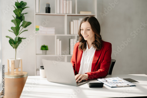 Confident business expert attractive smiling young woman typing laptop ang holding digital tablet on desk in creative home office.