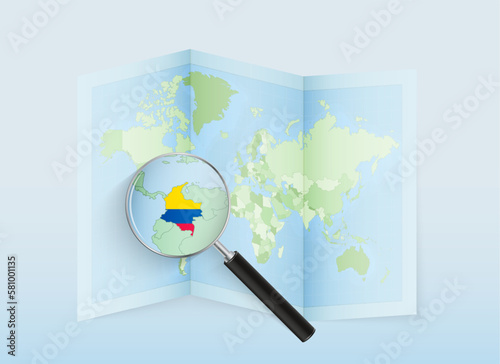 A folded world map with a magnifying lens pointing towards Colombia. Map and flag of Italy in loupe.