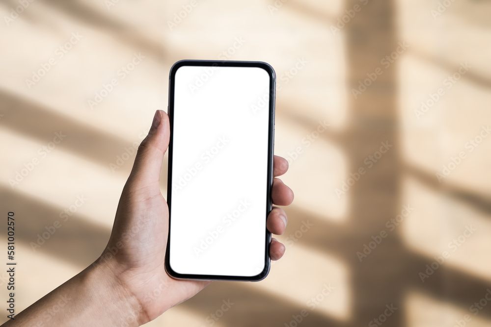 Hand holding white mobile phone with blank white screen in blur shadow background. Hand holding white mobile phone with blank white screen in blur shadow background.