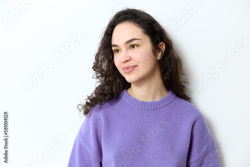 Portrait of young beautiful jewish girl with curly dark long hair wearing yellow eye shadow and purple knitted sweater smiling and looking away while standing isolated on white background in studio.
