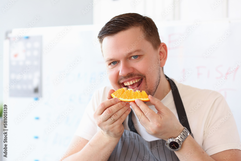 Red smiling male cook is biting orange Red smiling male cook is biting orange