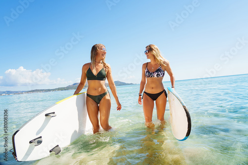  Portrait of young two smiling surfer womans on the beach holding her surfboard. Enjoy surfing on vacation.