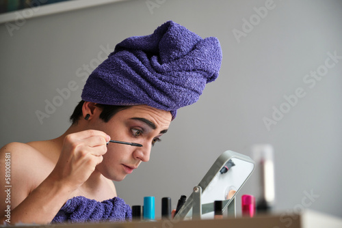 Young transgender man applying eye mascara.