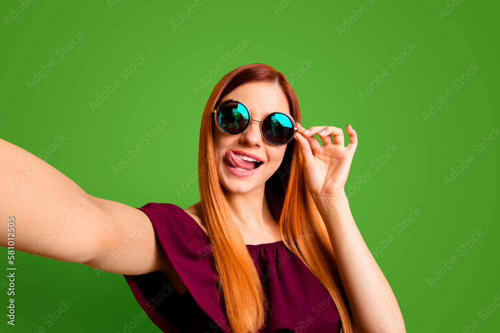 Close up portrait of happy woman in glasses making self portrait on front camera of smartphone isolated on yellow background