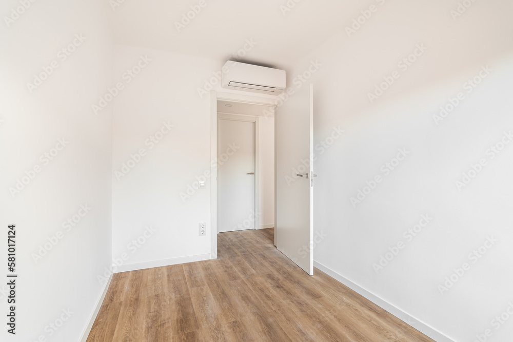 View of the front door to a small white air-conditioned room with wooden floor in a hotel. Concept of simple renovation or an empty apartment after move View of the front door to a small white air-conditioned room with wooden floor in a hotel. Concept of simple renovation or an empty apartment after move