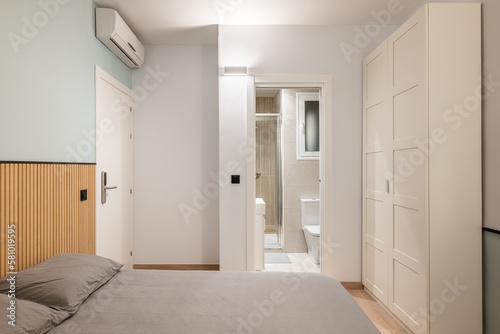 Double bed with gray linen  built-in wardrobe and air conditioning overlooking compact shower room. Concept of a small multifunctional apartment or hotel room