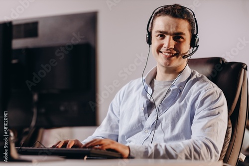 Smiling call center operator in blue shirt. Happy young man working as telesales marketer. Indoor shot of customer support agent photo