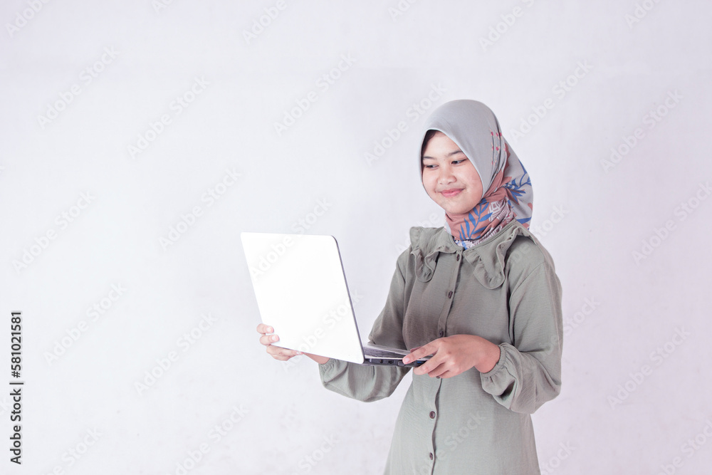 asian teen woman in hijab standing side view using white laptop studio isolated in plain white room, office lady concept. asian teen woman in hijab standing side view using white laptop studio isolated in plain white room, office lady concept.