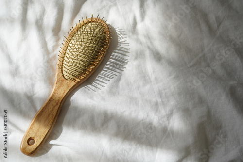 Wooden hairbrush on white bed background with shadows from window