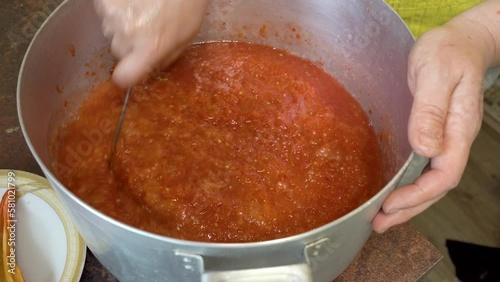prepare a spicy dish adjika,cook adjika in a saucepan, stir the dish with a spoon photo