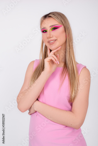 Well-groomed blonde with long straight hair and bright neon makeup to match dress smiles at camera. Creative image. 