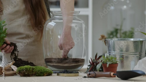 A young woman plants maidenhair in a glass terrarium for creating a tiny live forest ecosystem - close-up photo