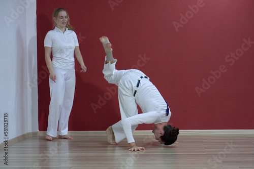 A mature man, a sports master, and a young woman, an aspiring athlete, practice the Brazilian martial art of capoeira in a small gym. photo