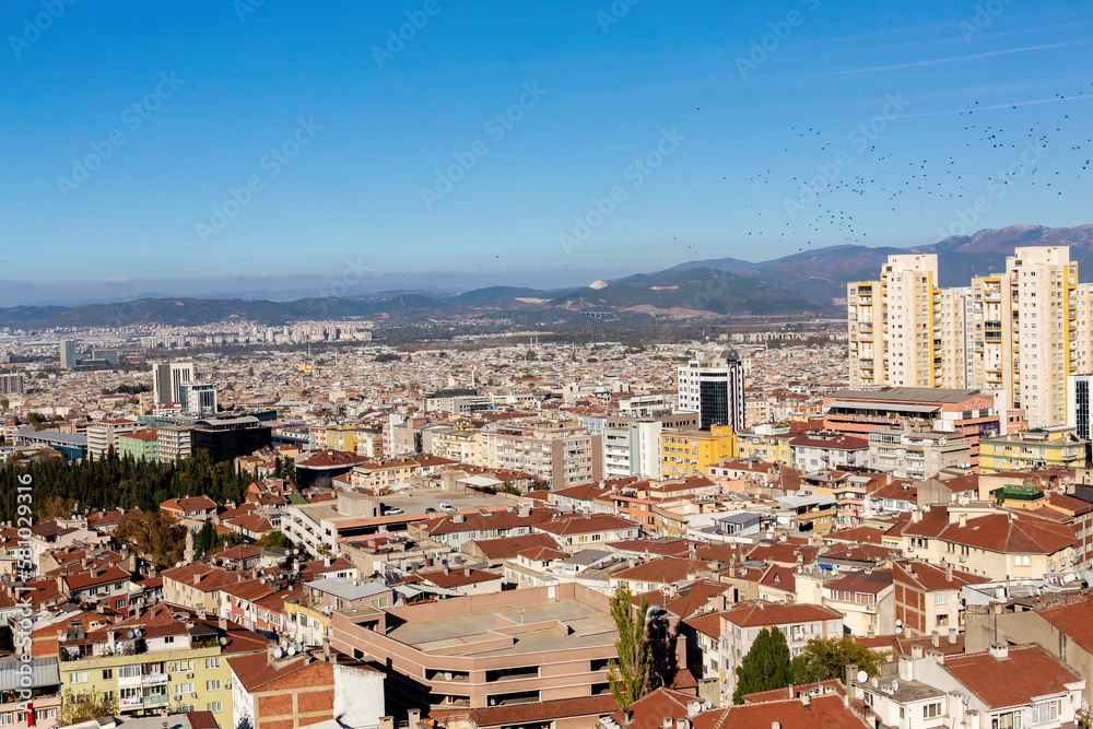 General view of Bursa City from Tophane. Bursa is the fifth biggest city in Turkey. Tiled roofs, city skyline and mountains at horizon, flock of birds at sky. Bursa, Turkey