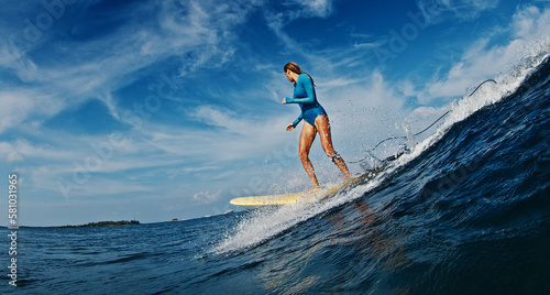 Slim woman surfer rides the wave. Woman surfs the ocean wave in the Maldives on yellow longboard © Dudarev Mikhail