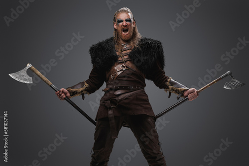 Studio shot of screaming viking with dual axes dressed in fur and leather armor.