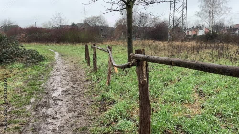 Small wooden fence made of tree trunks on a meadow with trees and small houses in the background Small wooden fence made of tree trunks on a meadow with trees and small houses in the background