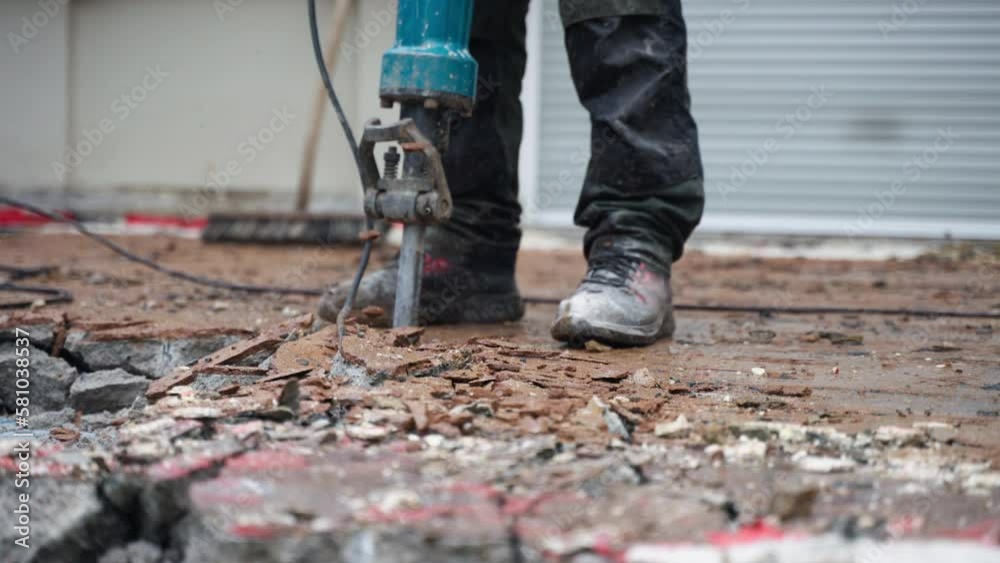 A construction worker using a jackhammer to remove old concrete near the house - close-up A construction worker using a jackhammer to remove old concrete near the house - close-up