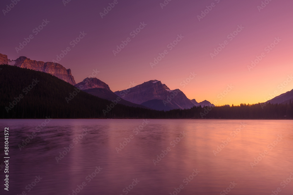 Lake and mountains in a valley at dawn. Reflections on the surface of the lake. Mountain landscape at sunrise. Natural landscape with bright sunshine. Alberta, Canada.
