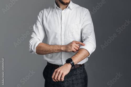 A man in a white shirt with rolled up sleeves is holding onto his collar. Watch on hand. Stylish business portrait of a man, close-up photo.