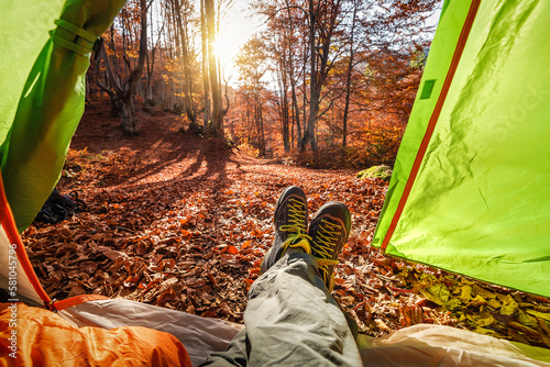 Legs in hiking shoes in tourist tent in nautumn forest photo