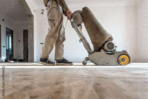 Professional carpenter grinding a wooden parquet floor by using floor sander in newly constructed house