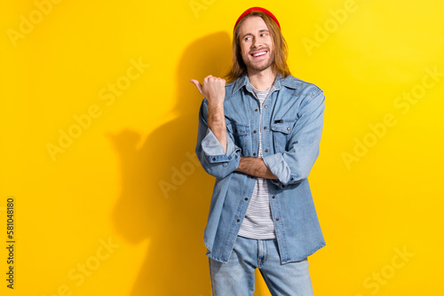 Photo of good mood funky guy with long hairdo dressed jeans shirt indicating at sale empty space isolated on yellow color background © deagreez