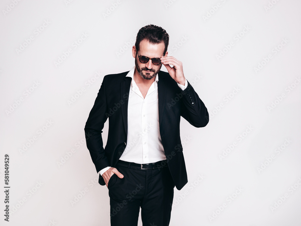 Portrait of handsome confident stylish hipster lambersexual model. Sexy modern man dressed in black elegant suit. Fashion male posing in studio, isolated on white. In sunglasses Portrait of handsome confident stylish hipster lambersexual model. Sexy modern man dressed in black elegant suit. Fashion male posing in studio, isolated on white. In sunglasses