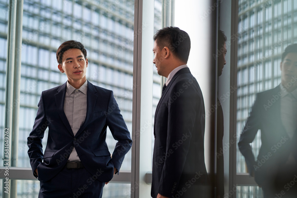two asian businesspeople talking chatting standing by the window talking chatting in office two asian businesspeople talking chatting standing by the window talking chatting in office
