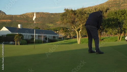 Golfer Taking Putt on the Putting Green at Sunrise with Mountains in the Background photo