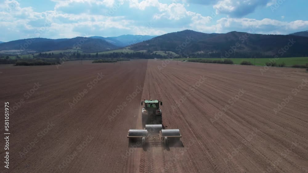 Rear aerial shot of Tractor pulling heavy rollers to flat large field, dolly in Rear aerial shot of Tractor pulling heavy rollers to flat large field, dolly in
