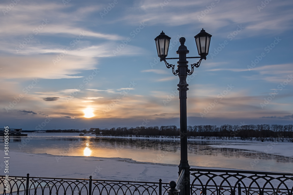 Street light on the city embankment on background of riverbank, cityscape and sunset sky at winter.