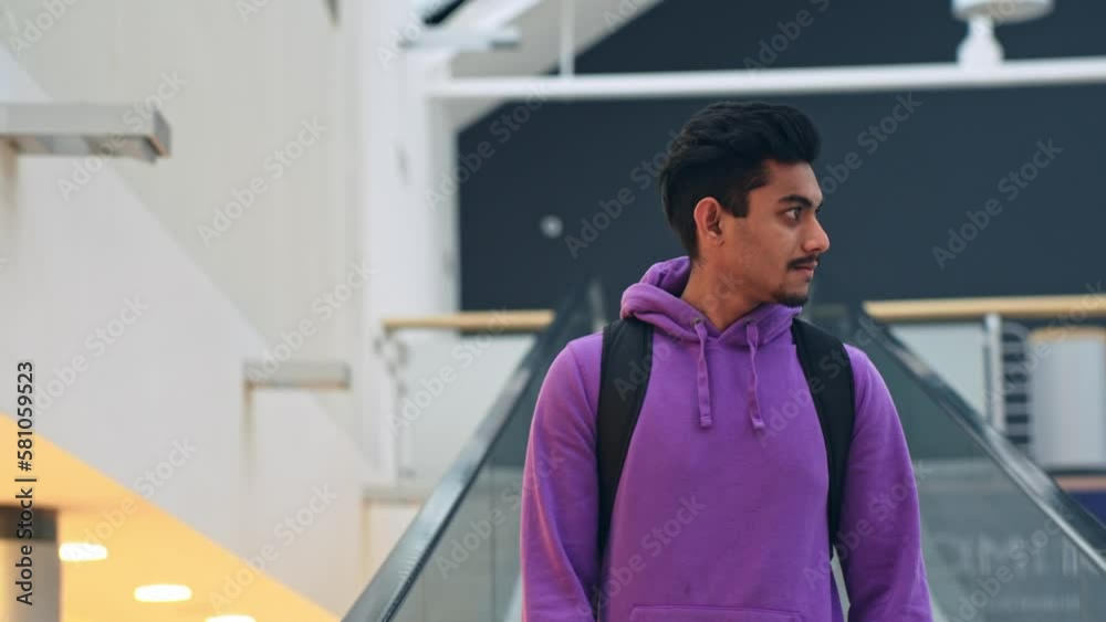 South Asian young man going down escalator at shopping center mall, static
