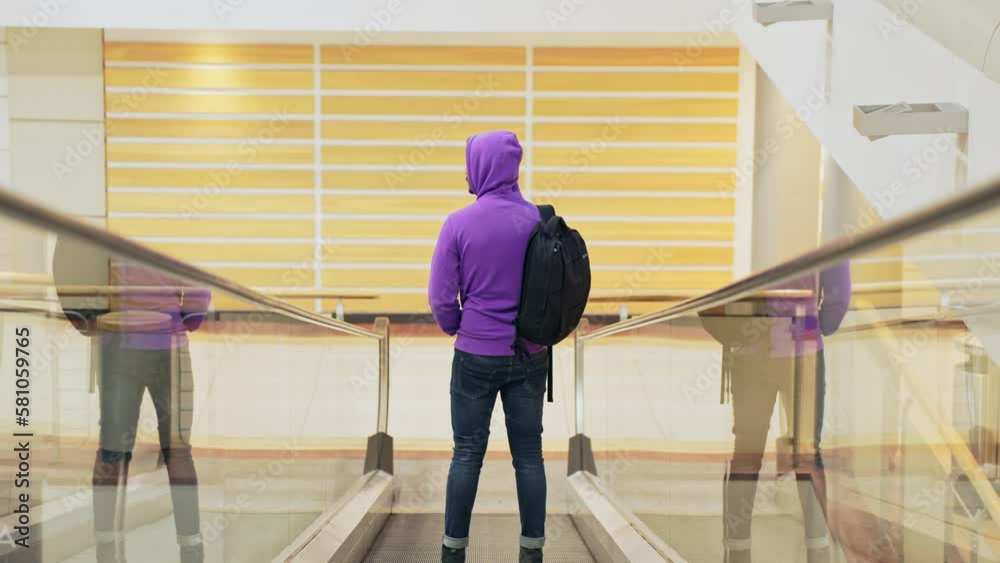 Fullshot of man standing on inclined moving walkways, wearing purple hoodie