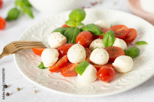 Italian caprese salad with sliced tomatoes, mozzarella, basil, olive oil on a light background.