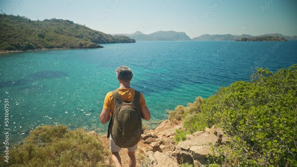 happy middle aged gray hair man traveler with backpack stands on cliff on shore of beautiful sea bay with clear turquoise water and paradise empty sea beach. slow motion 4k, travel in Turkey happy middle aged gray hair man traveler with backpack stands on cliff on shore of beautiful sea bay with clear turquoise water and paradise empty sea beach. slow motion 4k, travel in Turkey