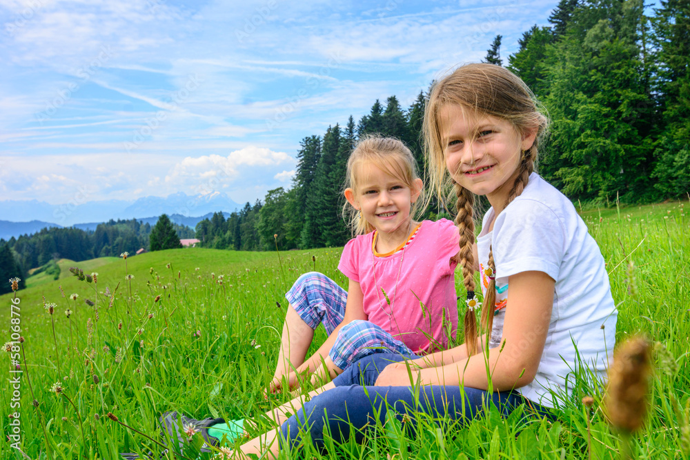 Zwei fröhliche Mädchen genießen unbeschwert Ihre Kindheit auf einer Bergwiese in Vorarlberg