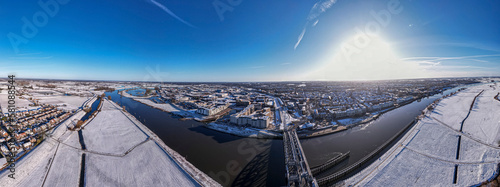 Panorama 180 degrees ready for VR with steel draw bridge over river IJssel and white floodplains of Dutch Hanseatic medieval tower town Zutphen, The Netherlands. Aerial cityscape after a snowstorm.