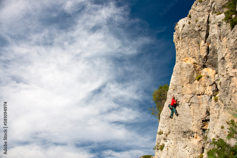 Young man climbing a limestone wall with wide valley in the background