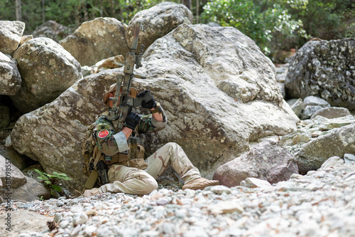 Homme militaire en uniforme à couvert derrière un gros rocher de granit. Rechargement d'arme, fusil, viseur, tir