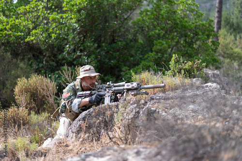 Homme militaire en uniforme en position de tir entre rochers de granit et végétation