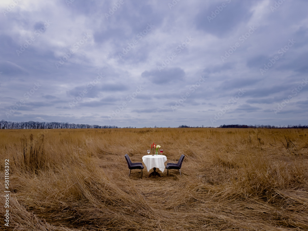 Obraz premium romantic date in nature. restaurant in the field.dinner in the wild. table with white tablecloth, chairs, glasses of wine, flowers and candles. without people 
