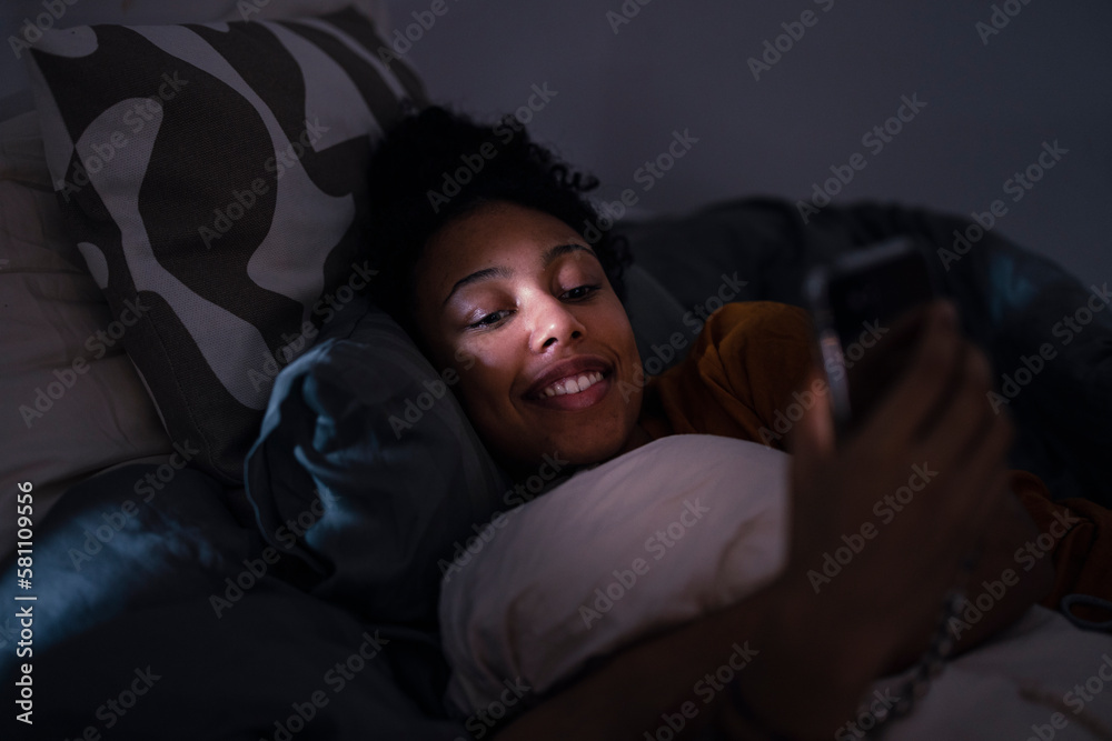 Smiling young woman using phone in bed Smiling young woman using phone in bed